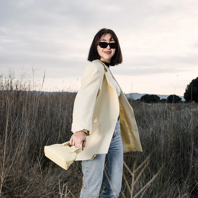 Marina Alves in a light blazer and sunglasses in a field at sunset